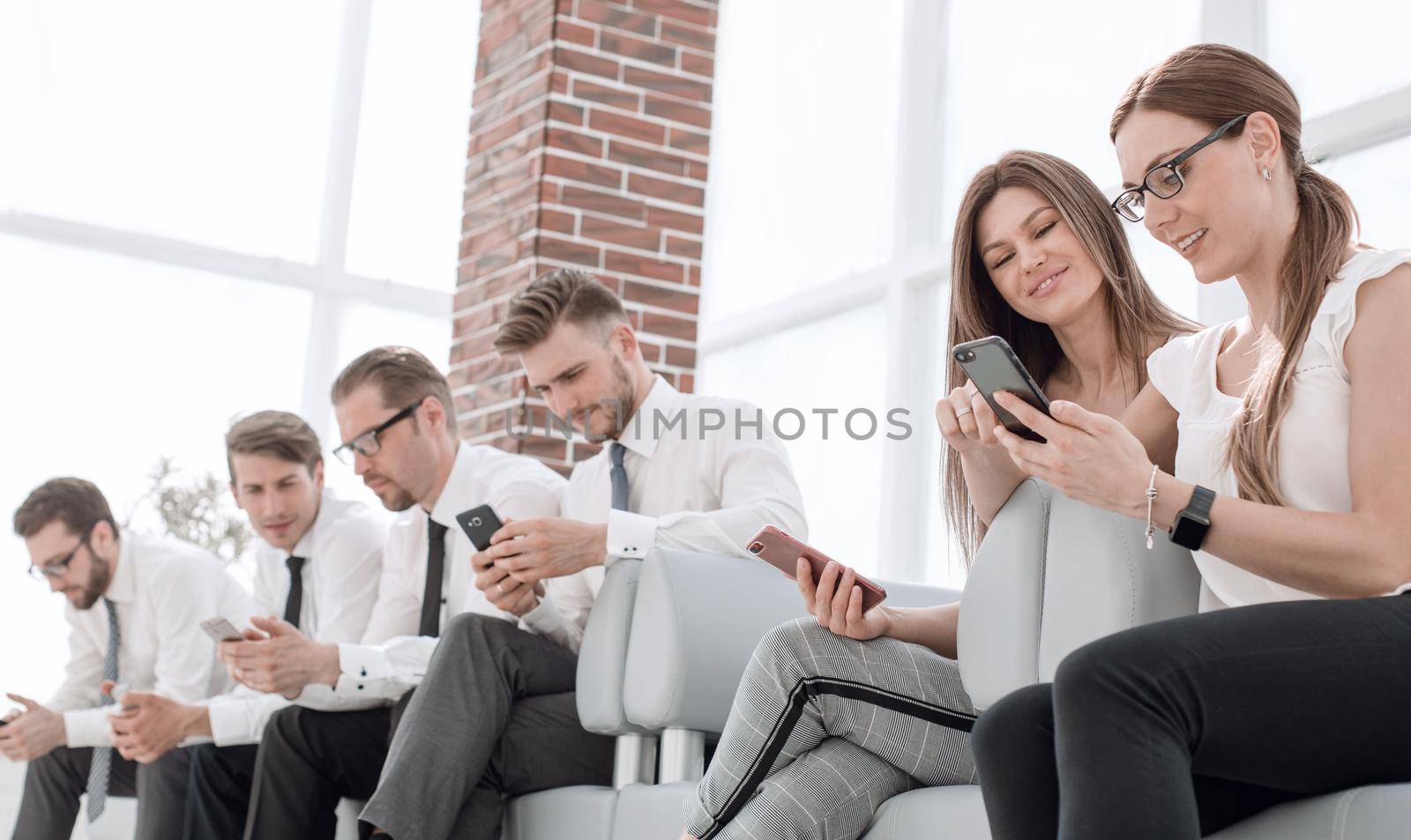 group of employees with gadgets sitting in the office waiting room by asdf