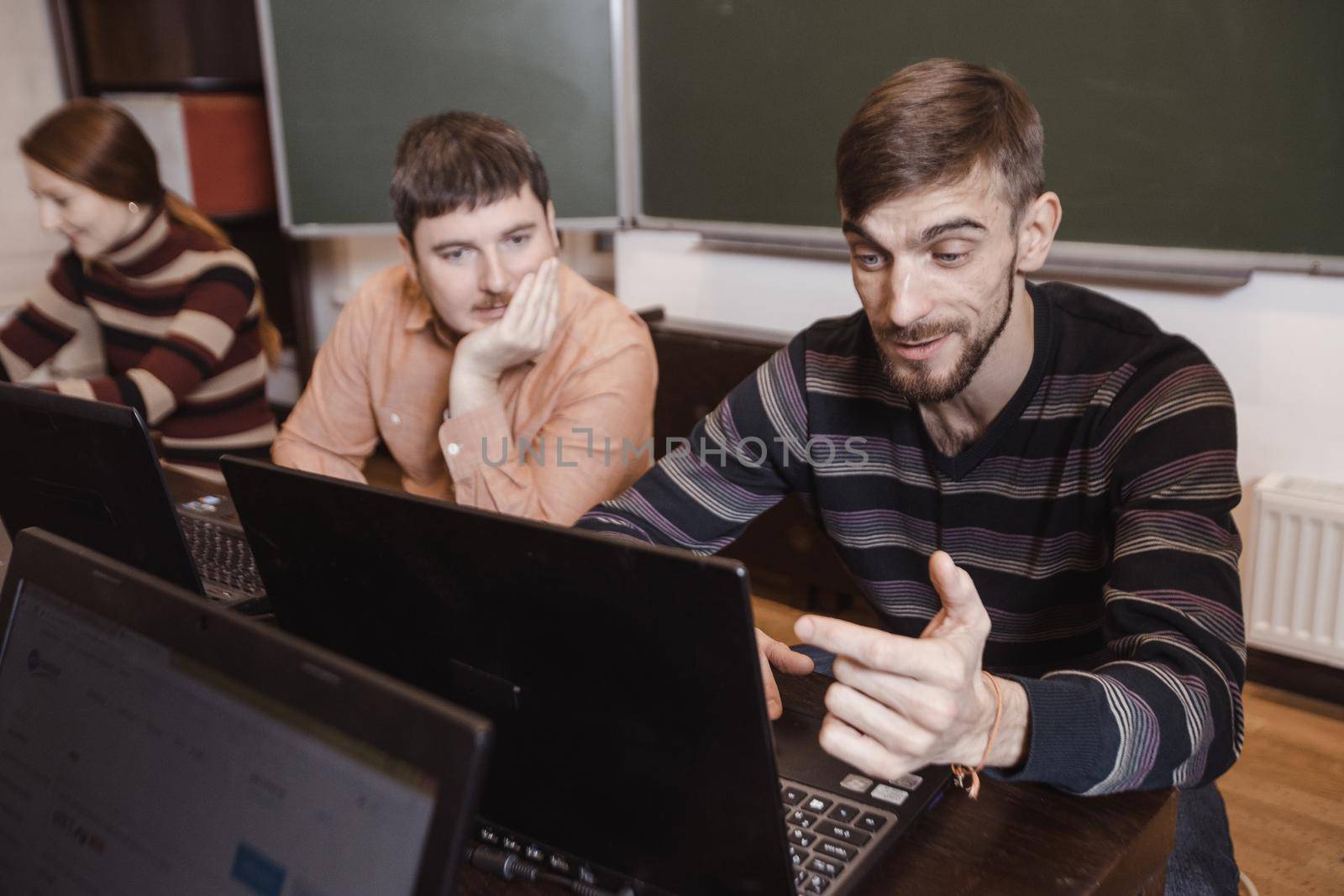 Young man watching laptop with astonishment while studying in class with other students.