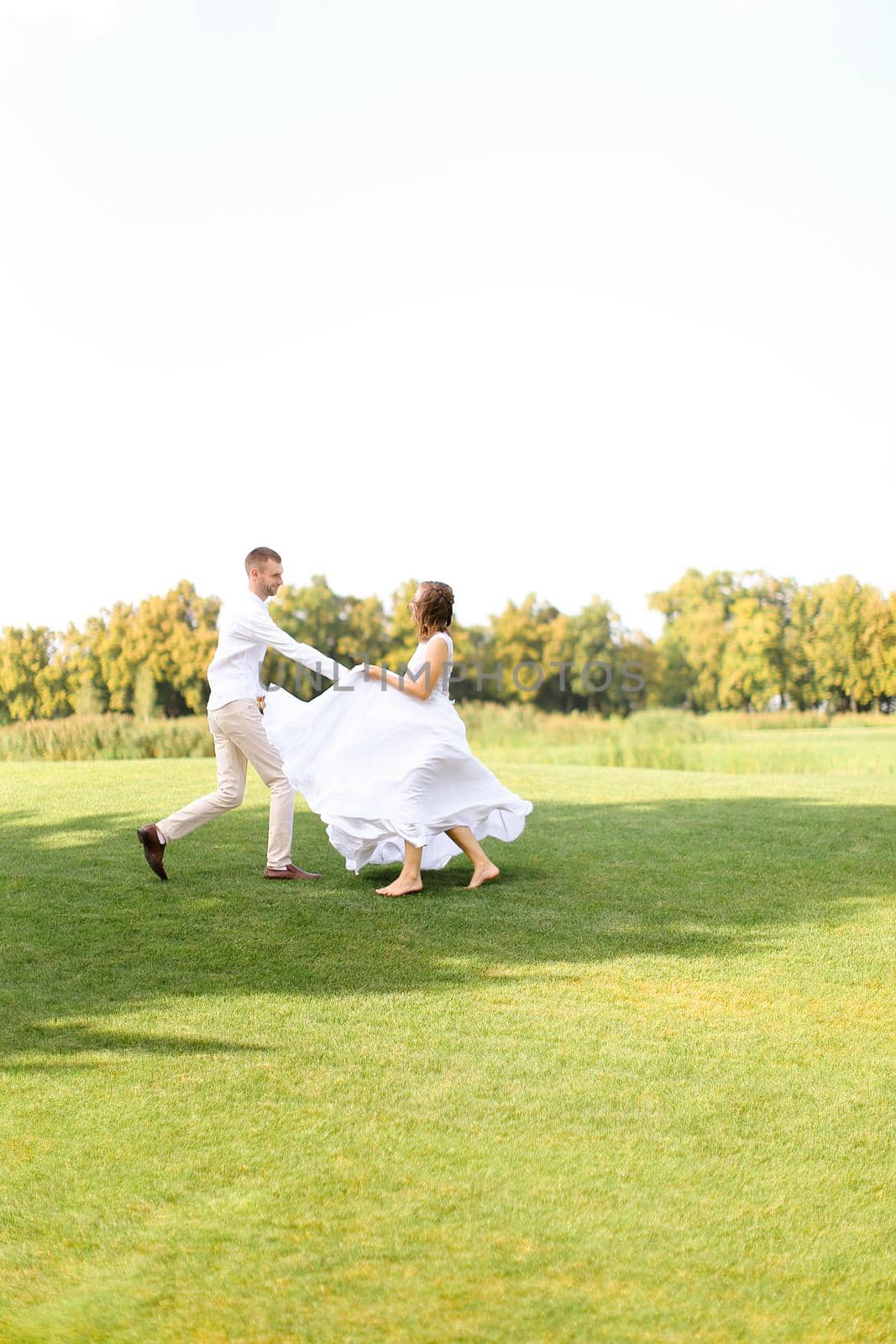Groom and bride dancing on grass. Concept of wedding photo session on open air and nature.