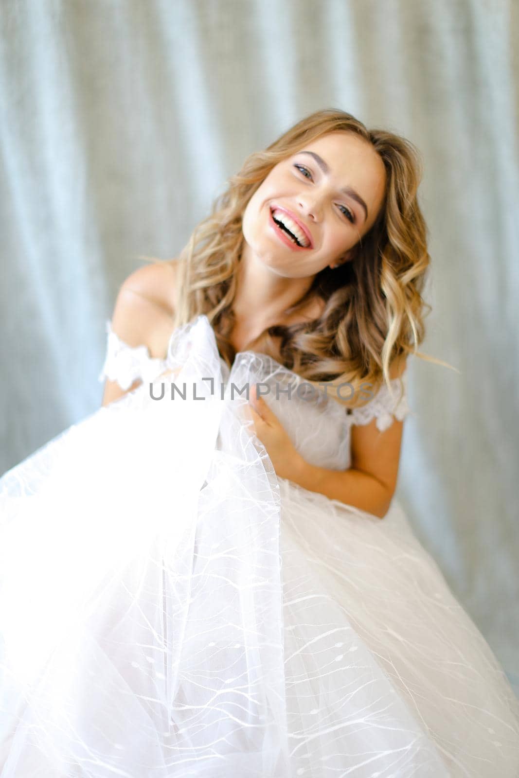 Young happy smiling bride wearing white dress at studio. Concept of bridal photo session and wedding fashion.