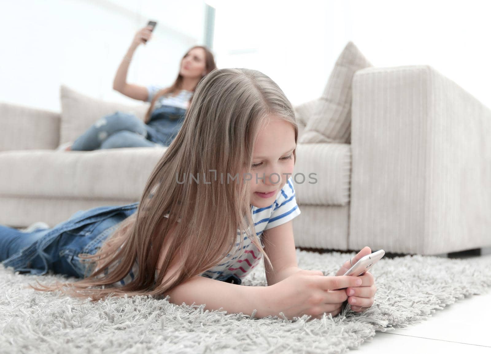 mom and her daughter using their smartphones in the new living room. by asdf