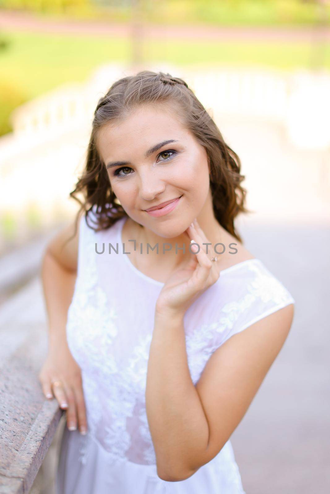 Happy caucasian bride wearing white dress standing outside and smiling. Concept of bridal photo session and wedding, nice fiancee.