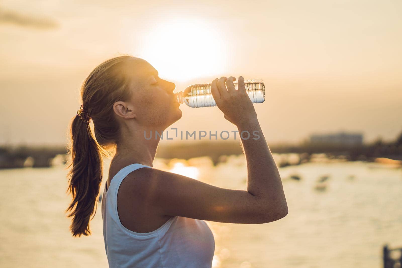 Sporty woman drinking water outdoor on sunny day by galitskaya
