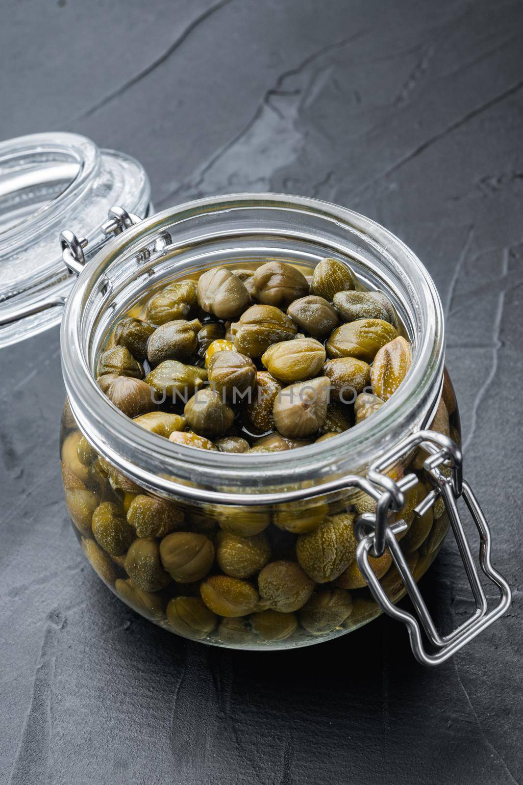 Baby capers in glas jar, on black background
