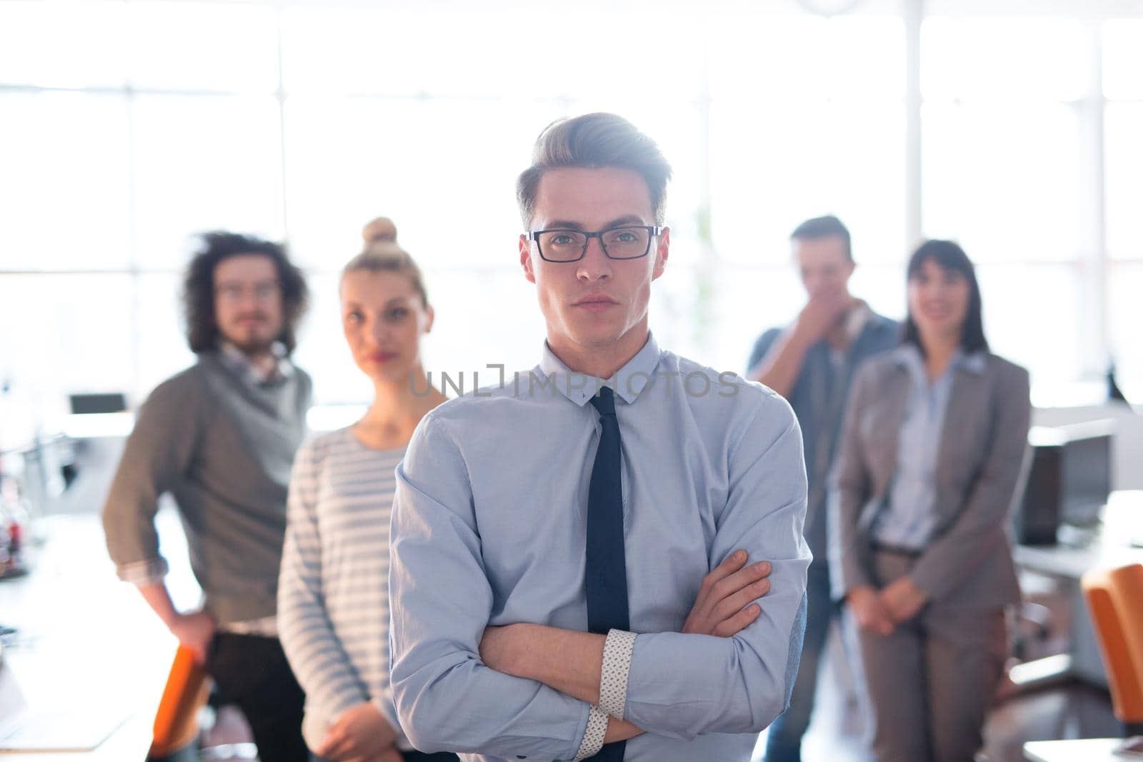 Portrait of smiling young casuall businessman with colleagues in background at the office