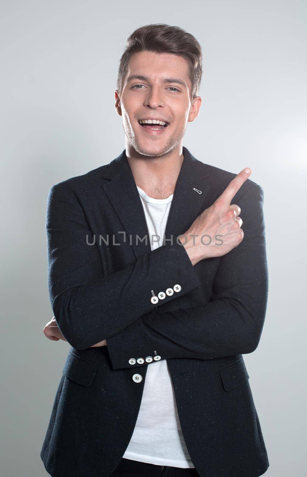 Close up portrait of young successful brunete stock-market broker guy on the gray background, he is smiling and is pointing on a copyspace with his finger