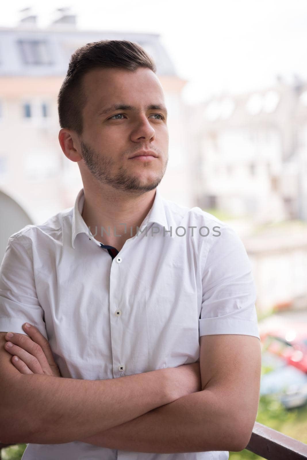 young elegant fashion man standing at balcony with arms crossed and smiling