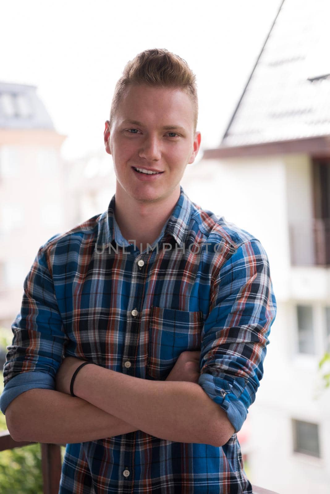 young elegant fashion man standing at balcony with arms crossed and smiling