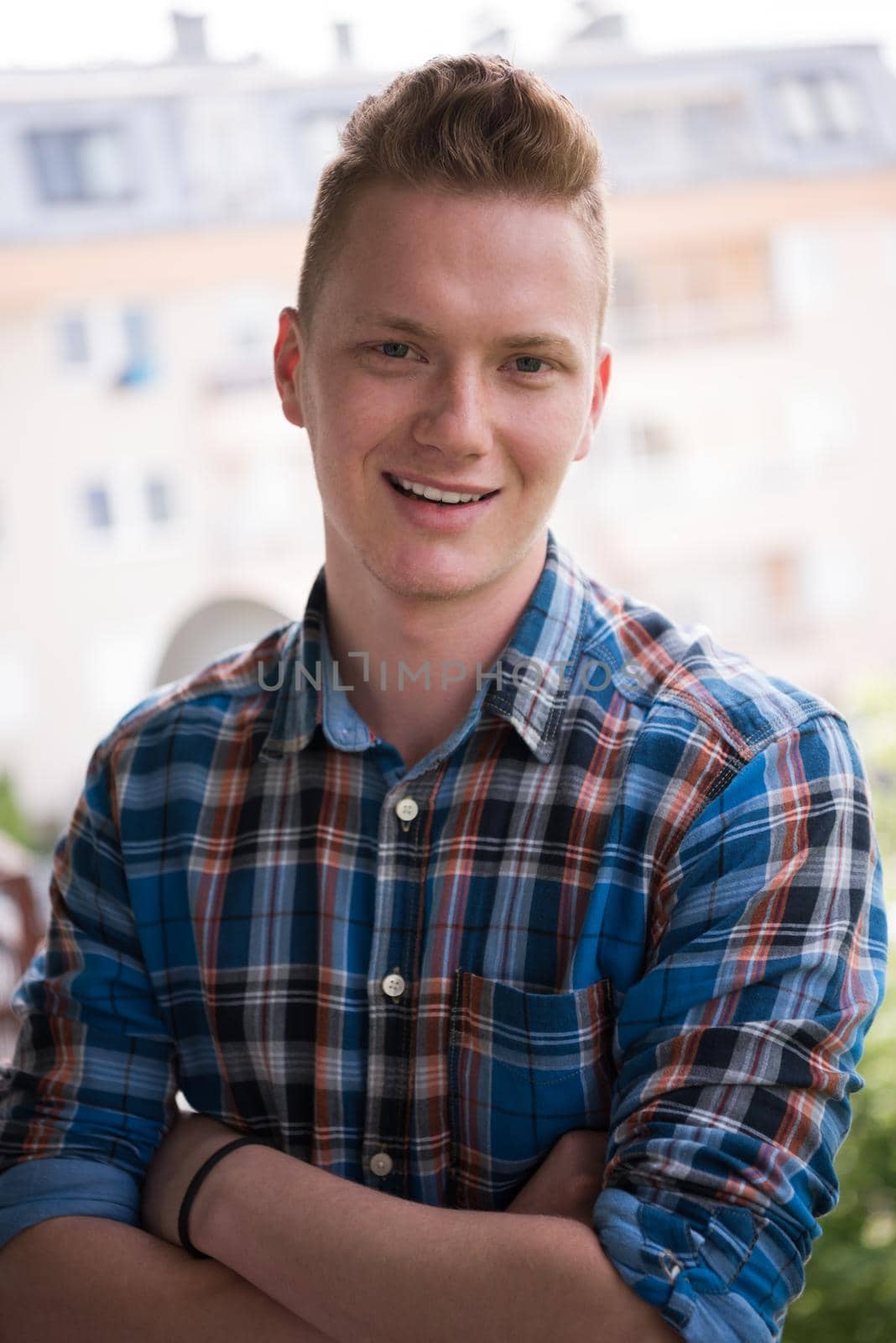 young elegant fashion man standing at balcony with arms crossed and smiling