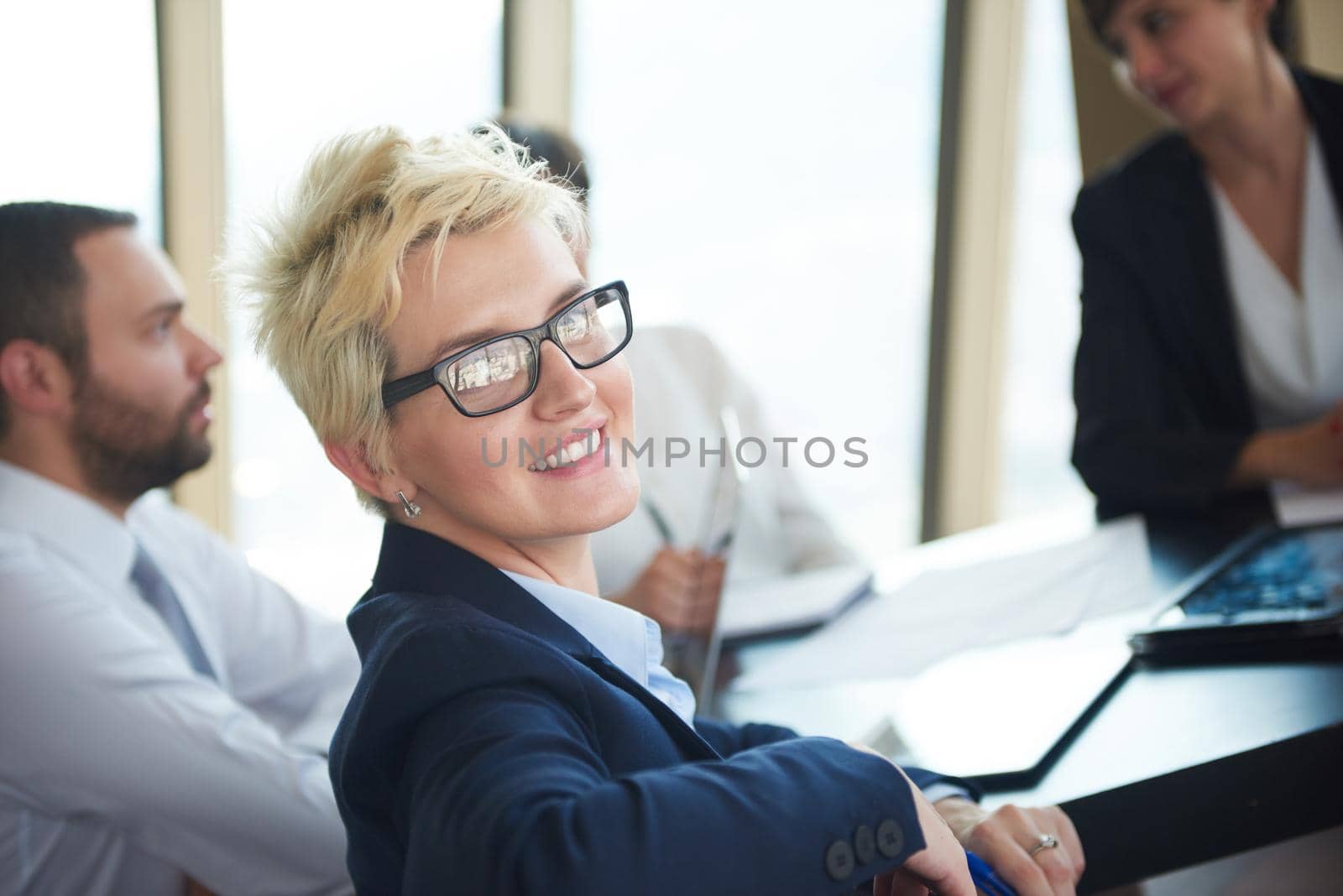 blonde with short hairstyle  and glasses,  business woman on meeting, people group in background at modern bright office indoors