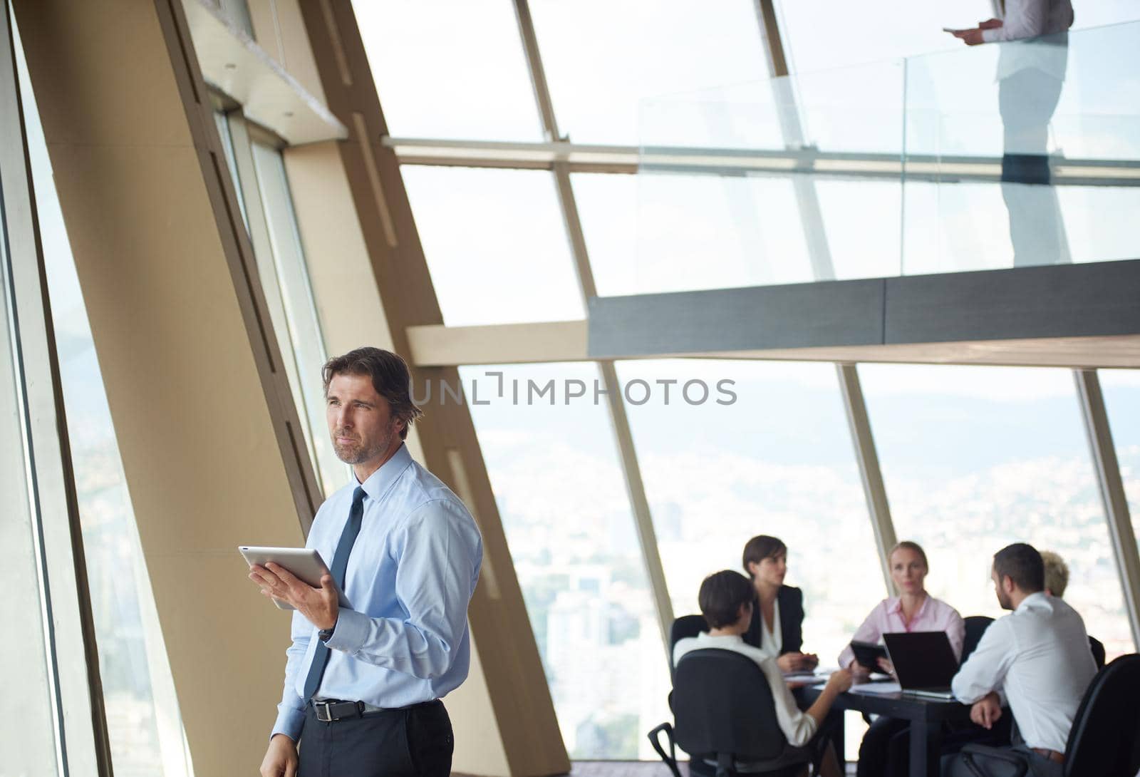 handosme business man working on tablet computer at modern bright office indoors with his team in group working together in background