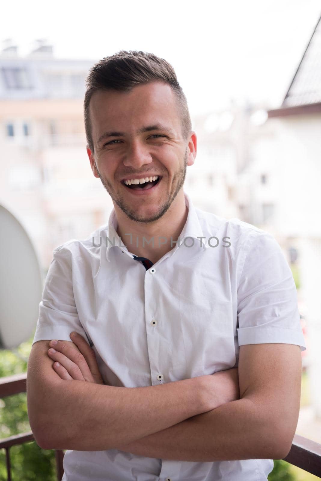 young elegant fashion man standing at balcony with arms crossed and smiling