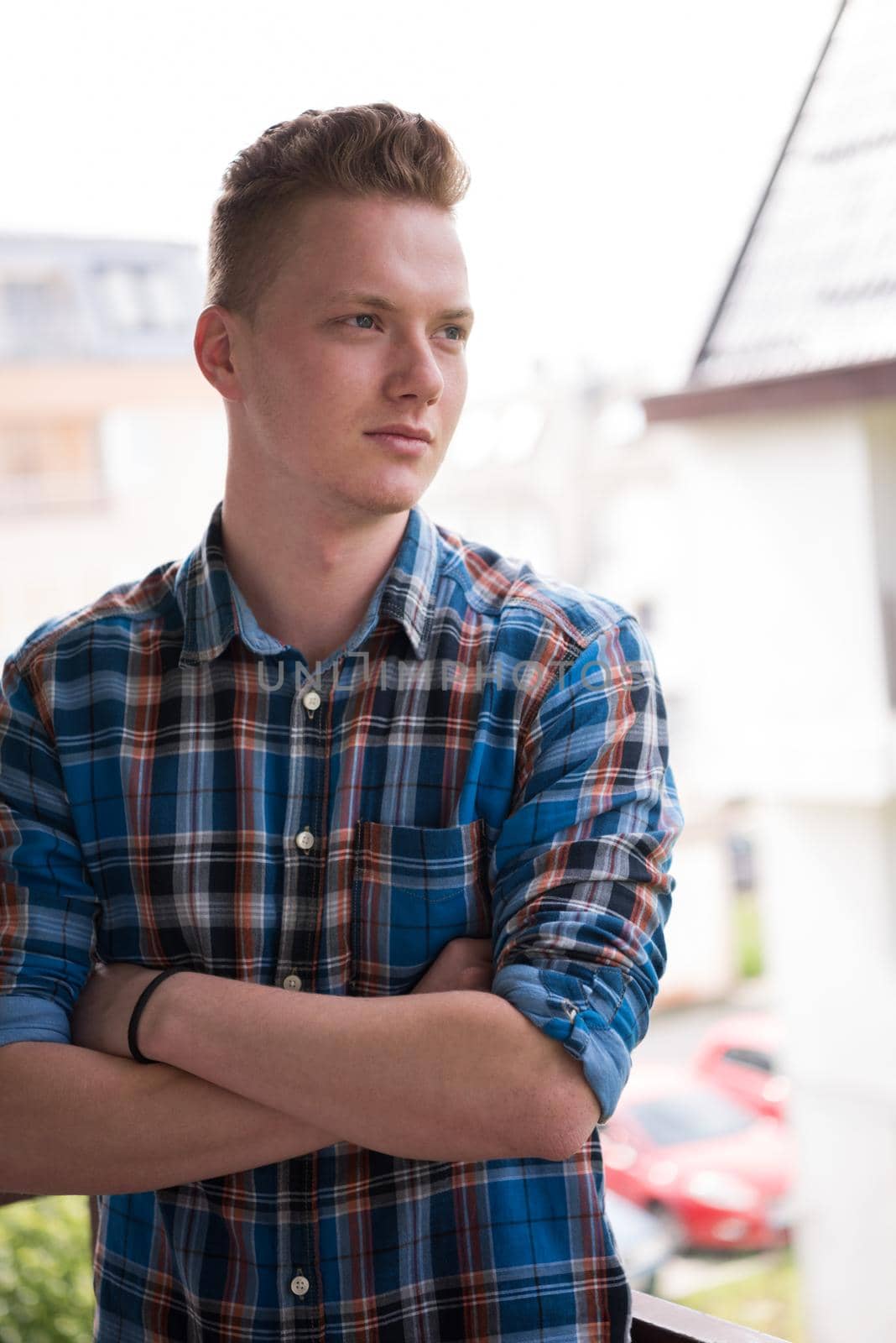 young elegant fashion man standing at balcony with arms crossed and smiling