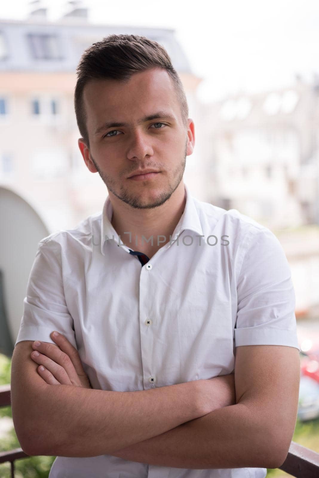 young elegant fashion man standing at balcony with arms crossed and smiling