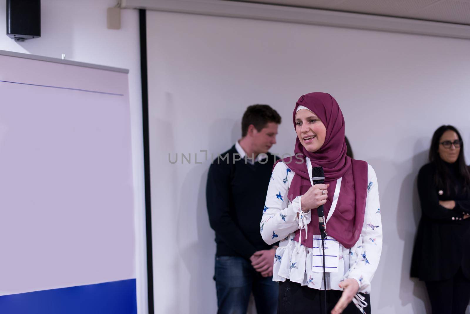 young muslim businesswoman with red scarf at business conference room giving public presentations. Audience at the conference hall. Entrepreneurship club