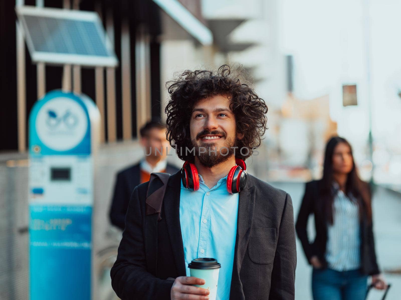 Happy student with afro haircut walking on campus while wearing his manbag and his headphones.