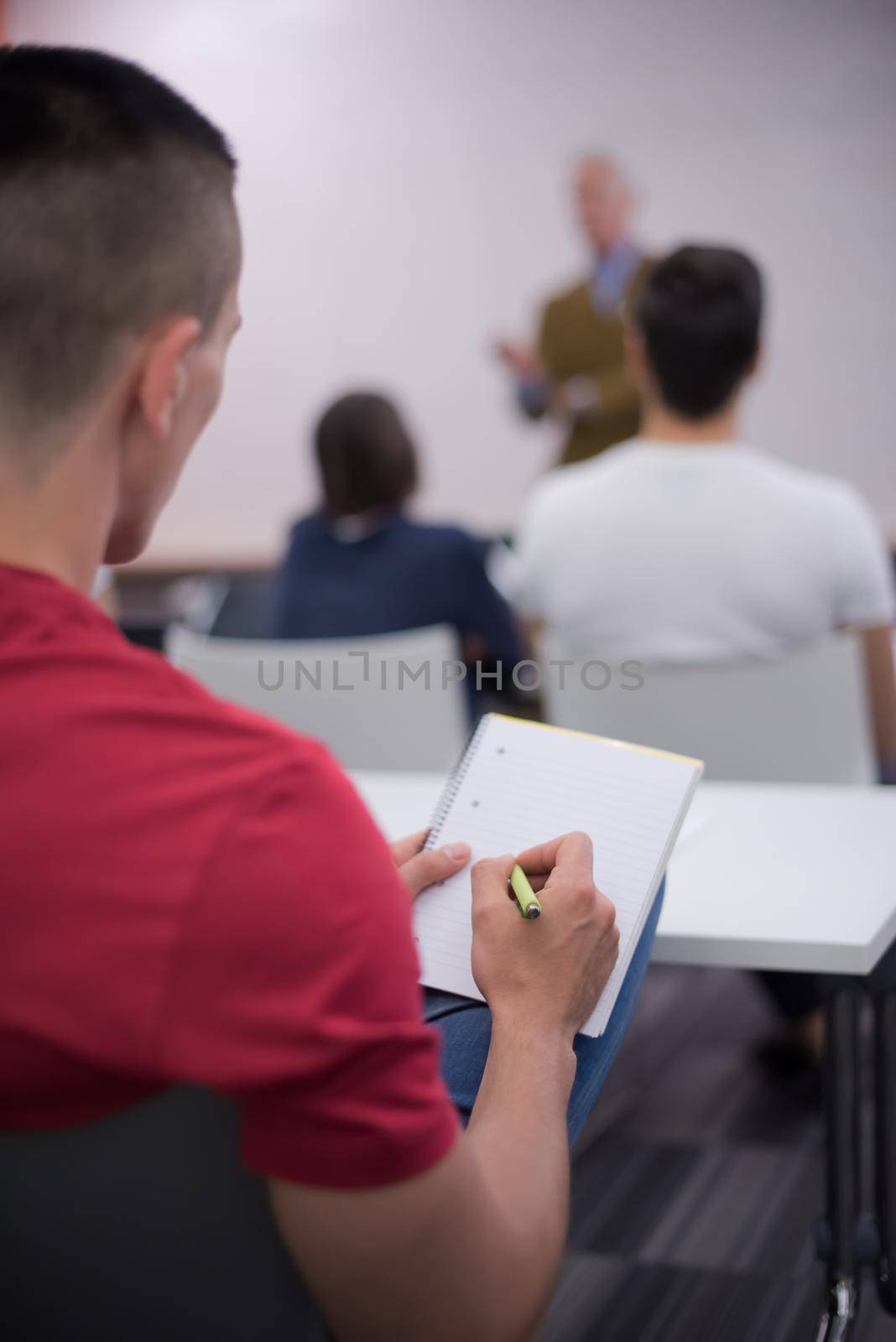 male student taking notes in classroom by dotshock