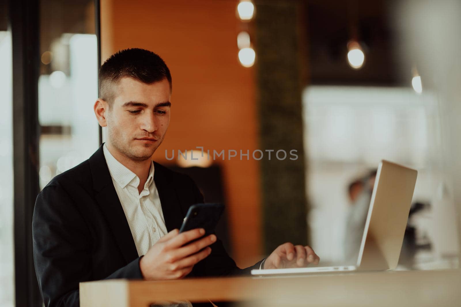 Happy businessman sitting at the cafeteria with laptop and smartphone. Businessman texting on smartphone while sitting in a pub restaurant. Businessman working and checking email on the computer.