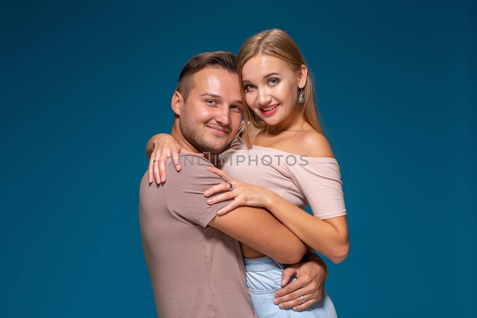 Young couple is hugging on blue background in studio. They wear T-shirts, jeans and smile. Friendship, love and relationships concept