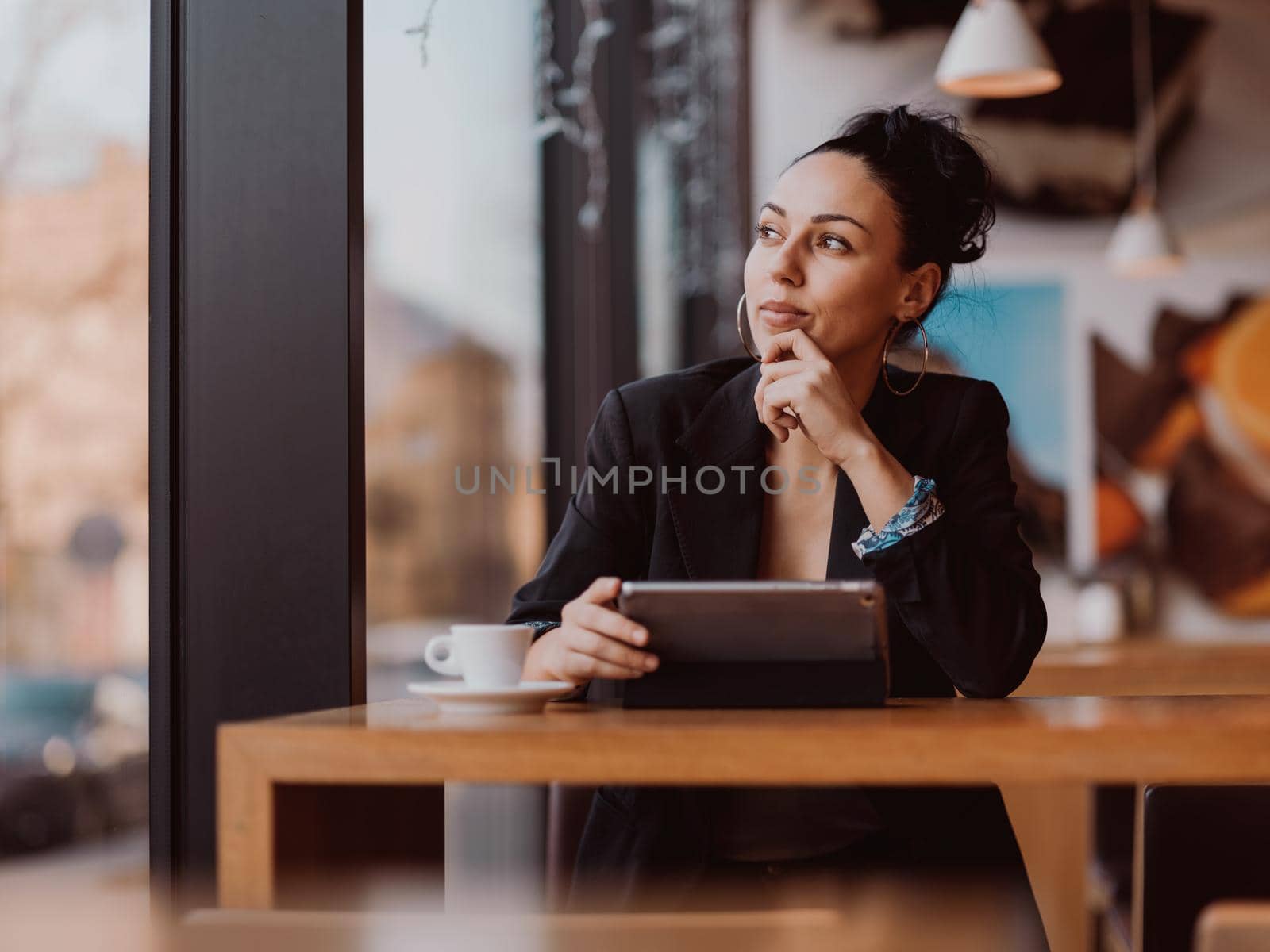 Latina woman sitting in cafe using tablet and drinks coffee on break from work