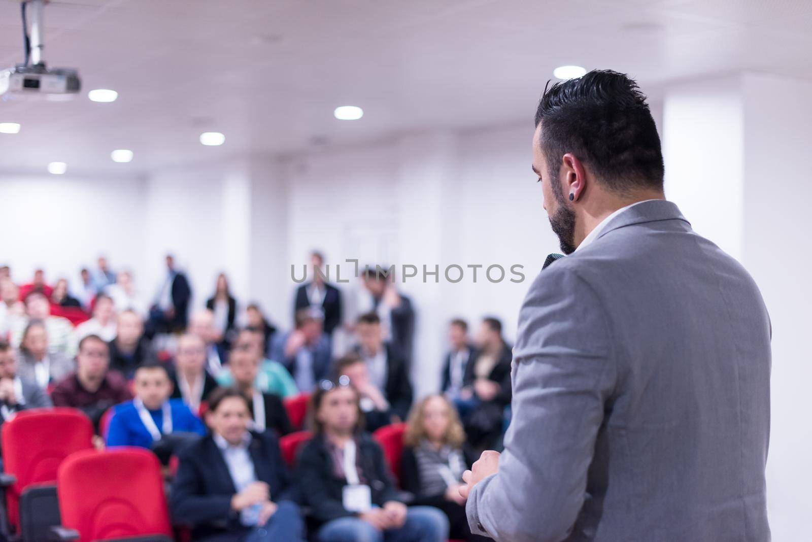 rear view of young successful businessman at business conference room with public giving presentations. Audience at the conference hall. Entrepreneurship club