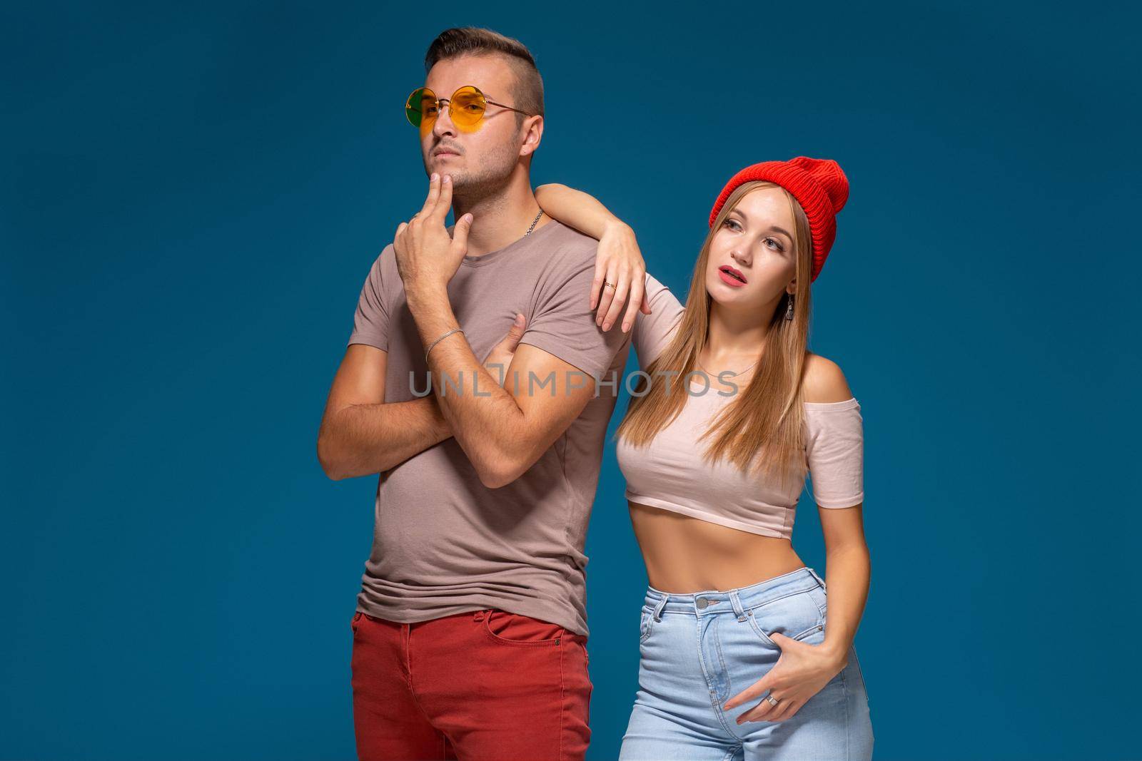 Studio lifestyle portrait of two best friends hipster wearing stylish bright outfits, hats, denim shorts and glasses, going crazy and having great time together. Indoor studio shot, isolated on blue background.