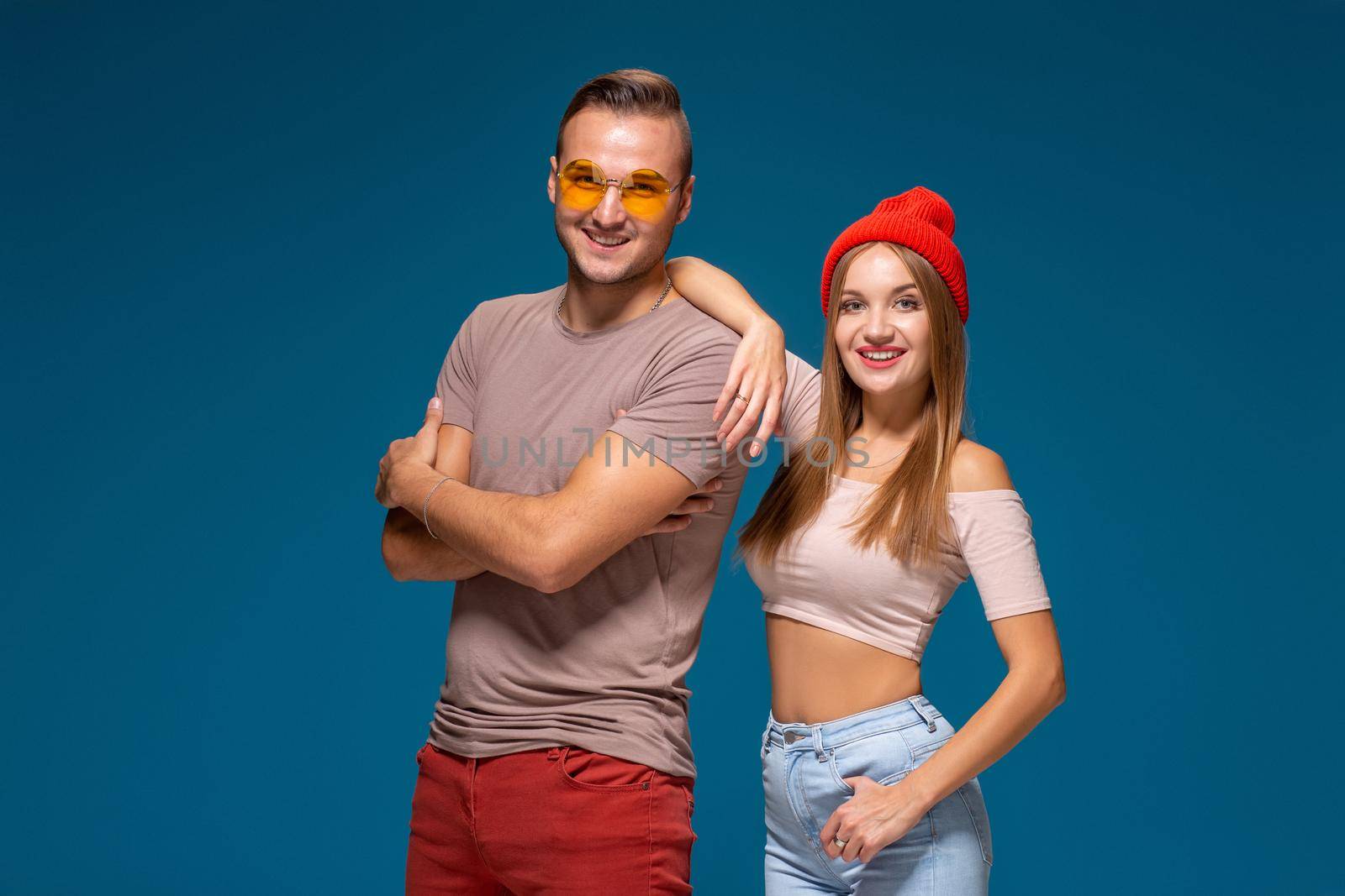 Studio lifestyle portrait of two best friends hipster wearing stylish bright outfits, hats, denim shorts and glasses, going crazy and having great time together. Indoor studio shot, isolated on blue background.