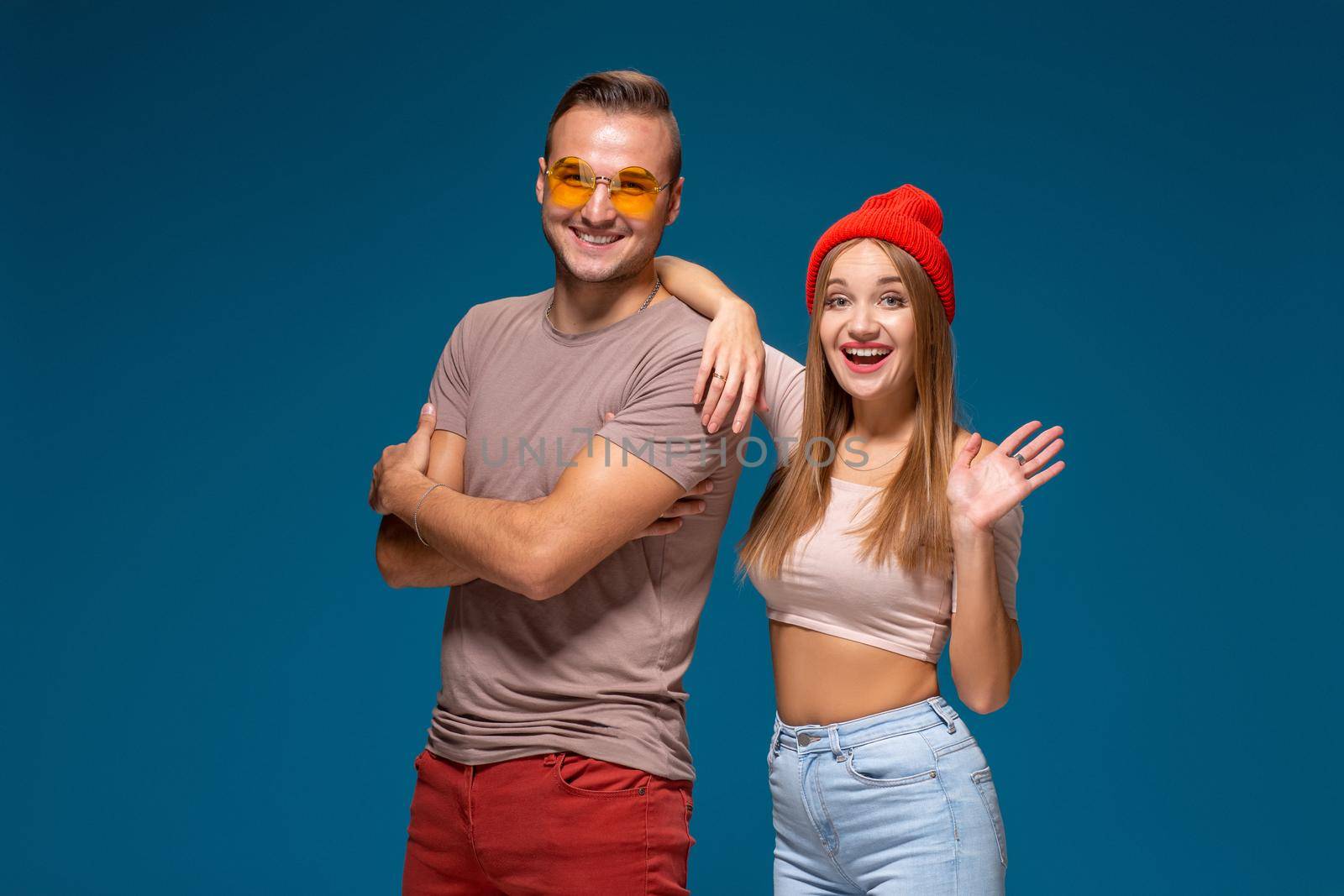 Studio lifestyle portrait of two best friends hipster wearing stylish bright outfits, hats, denim shorts and glasses, going crazy and having great time together. Indoor studio shot, isolated on blue background.