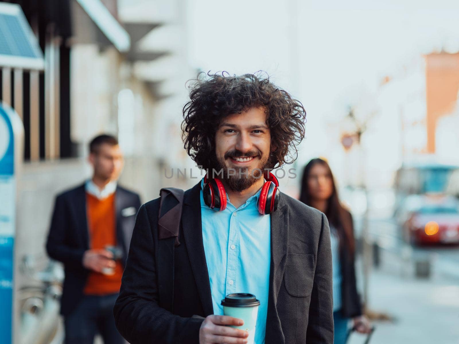 Happy student with afro haircut walking on campus while wearing his manbag and his headphones.