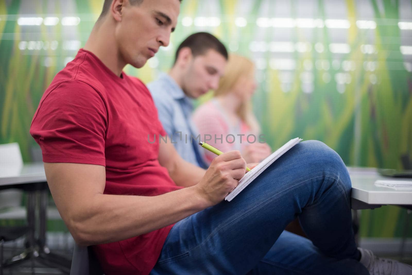 male student taking notes in classroom by dotshock