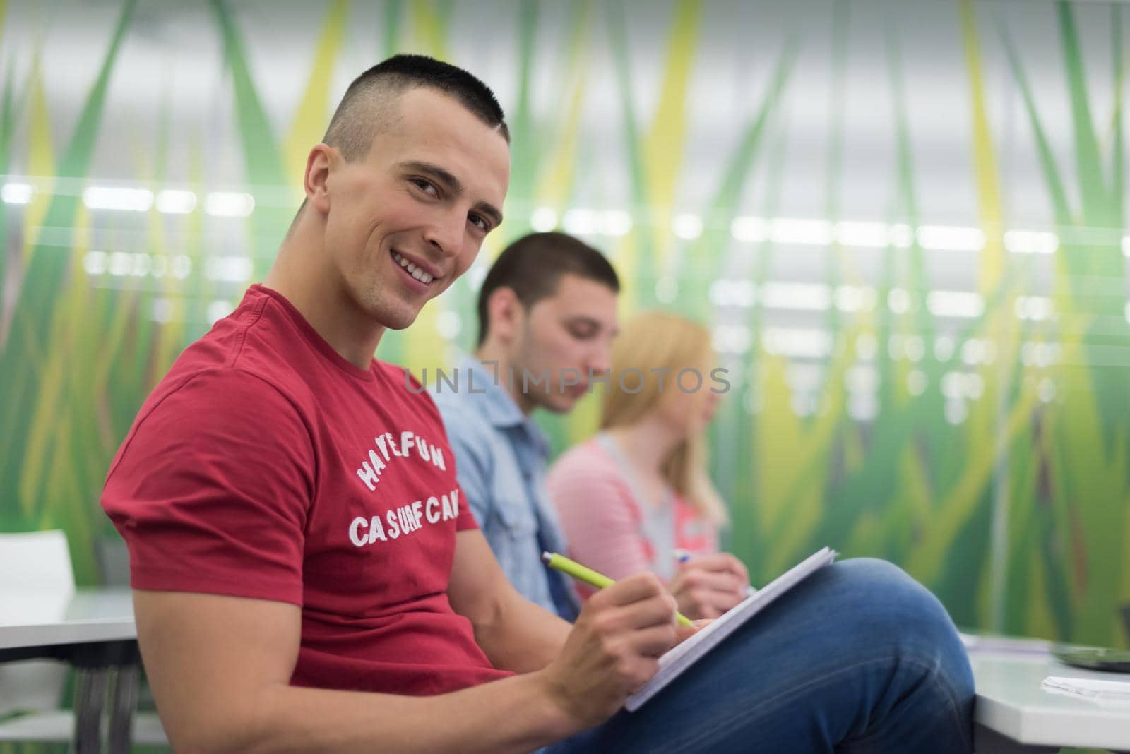 male student taking notes in classroom by dotshock