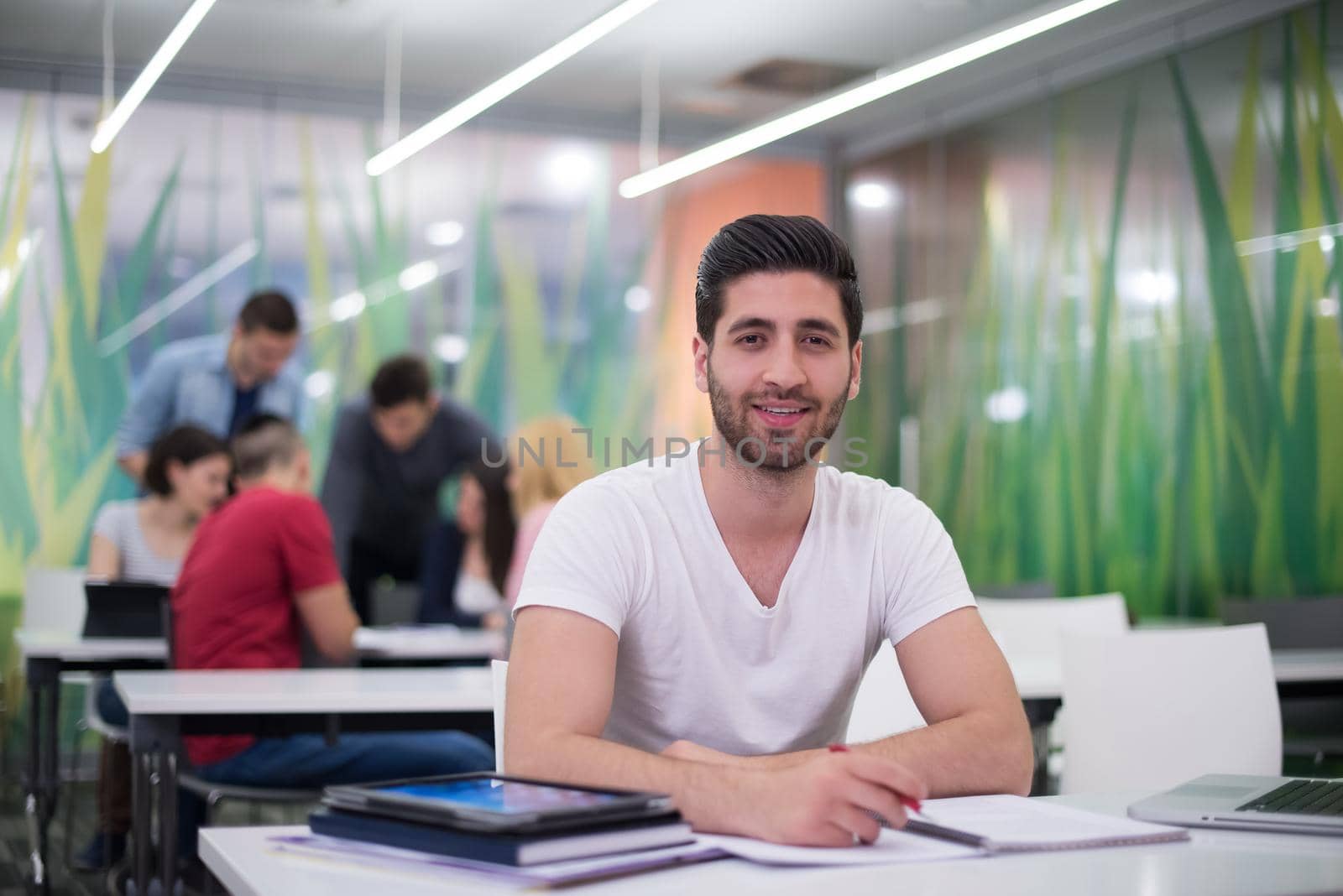 male student in classroom working  homework  and learning with laptop computer, students group in background