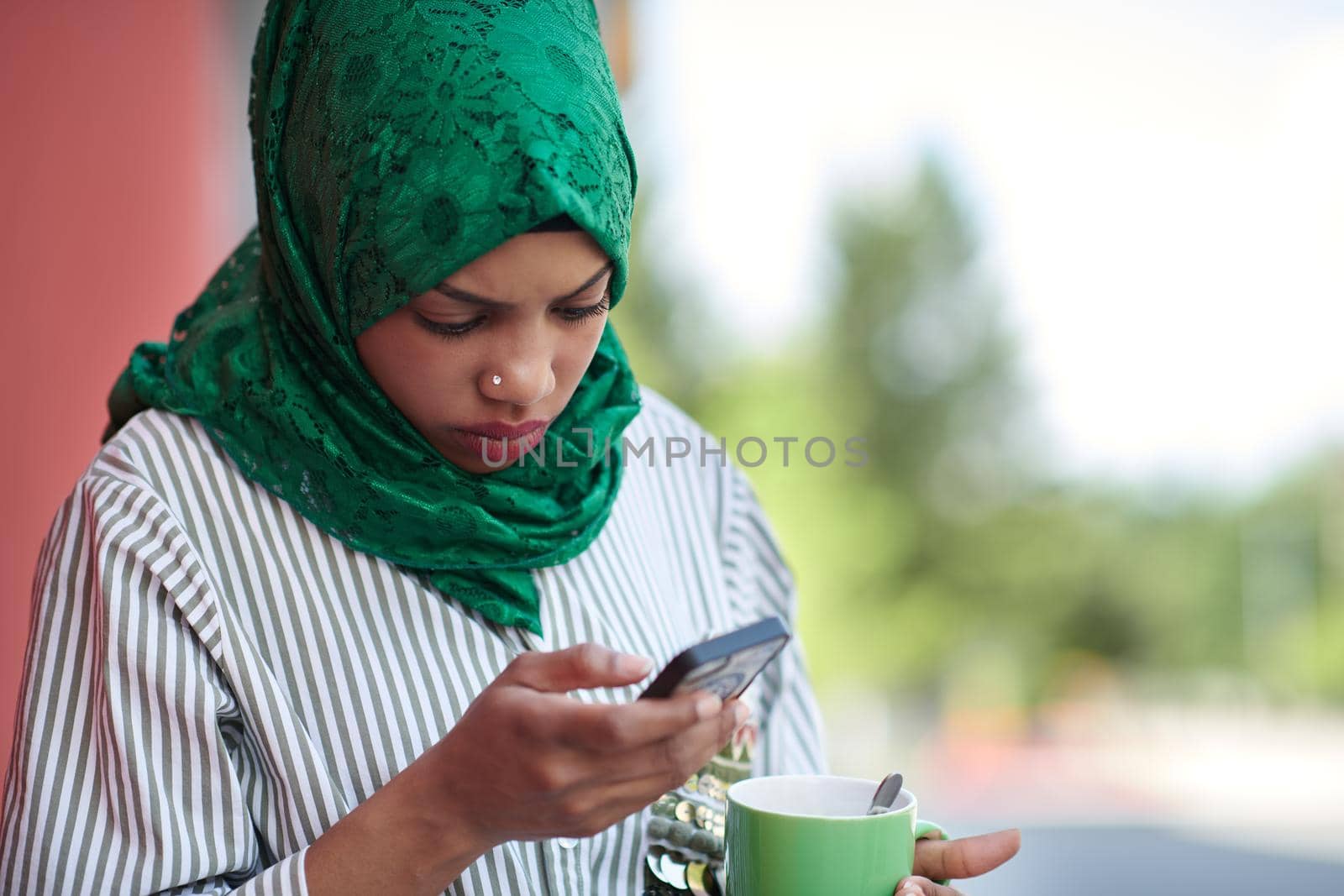 african muslim businesswoman with green hijab using mobile phone during coffee break from work outside