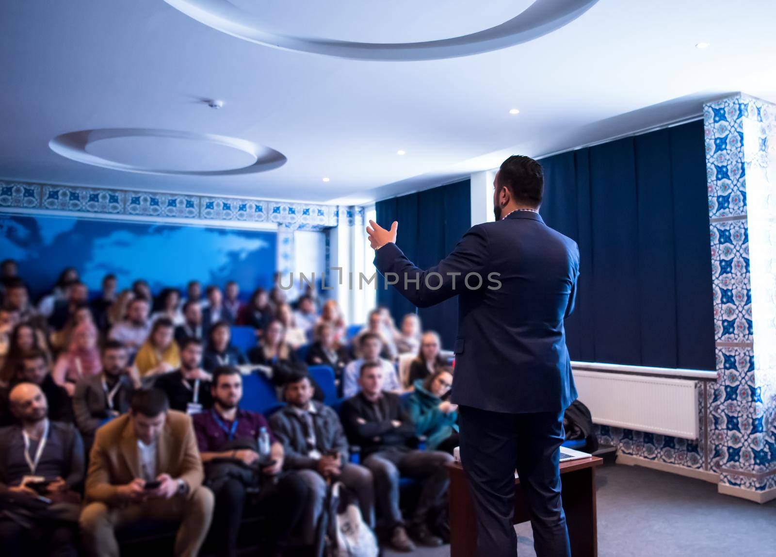 rear view of young successful businessman at business conference room with public giving presentations. Audience at the conference hall. Entrepreneurship club