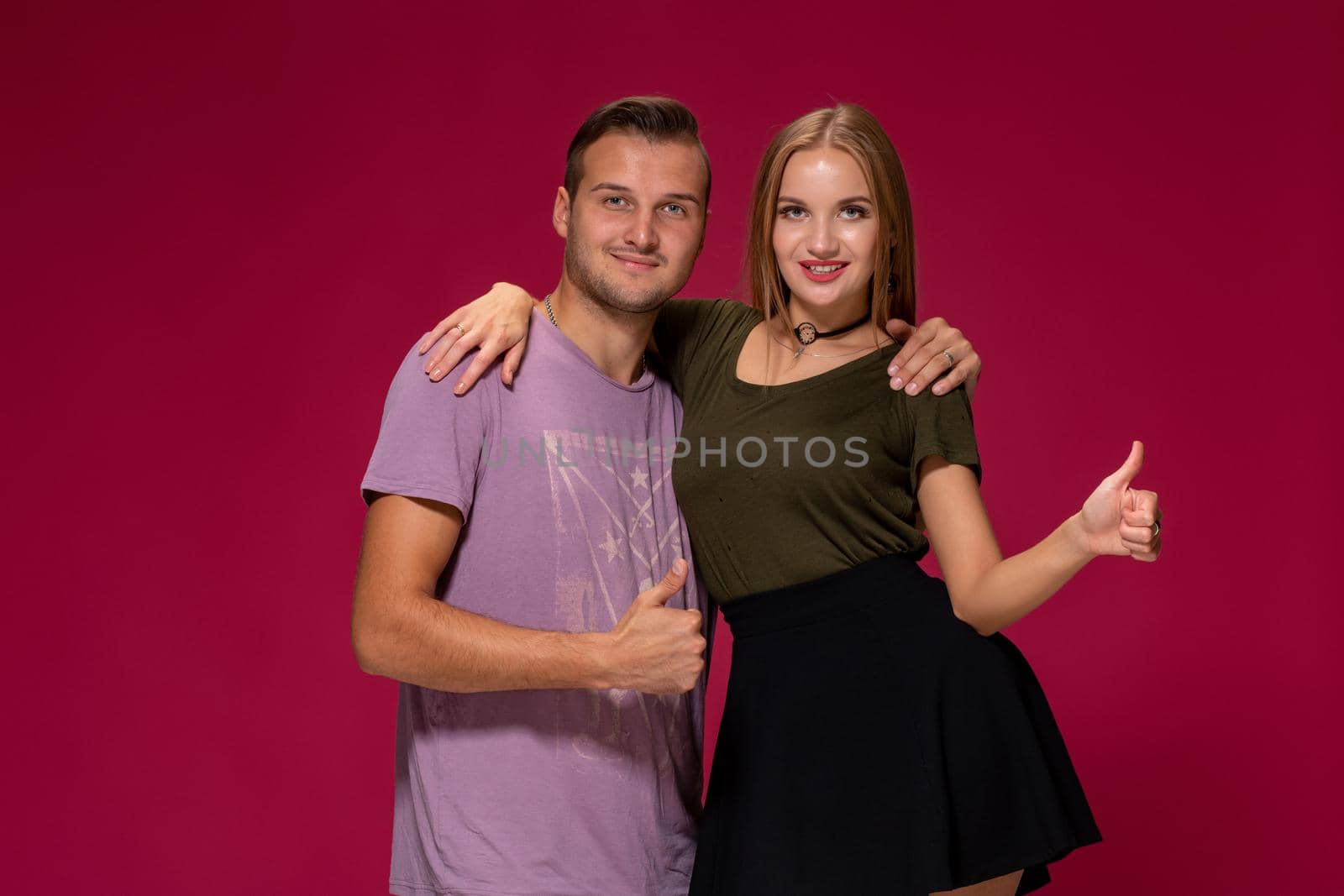 People, friendship, love and leisure concept - lovely couple with thumbs-up gesture on burgundy background with copy space for your advertisement or written text.