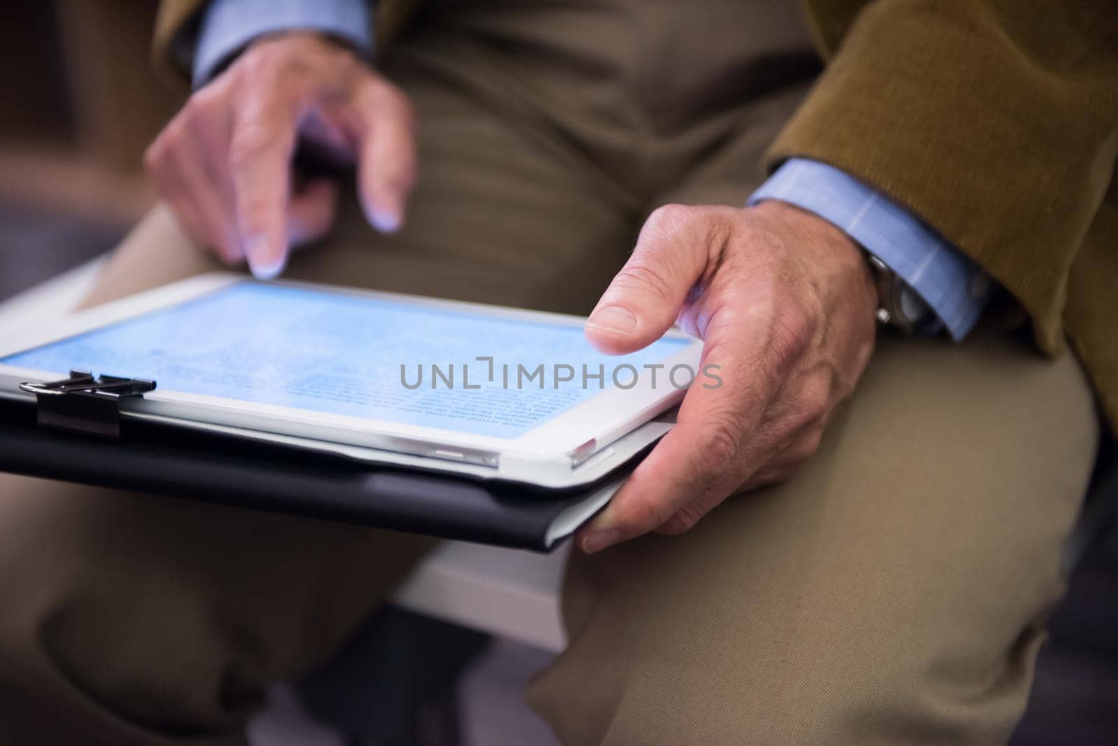Closeup of mature hands holding tablet. Teacher with students in classroom