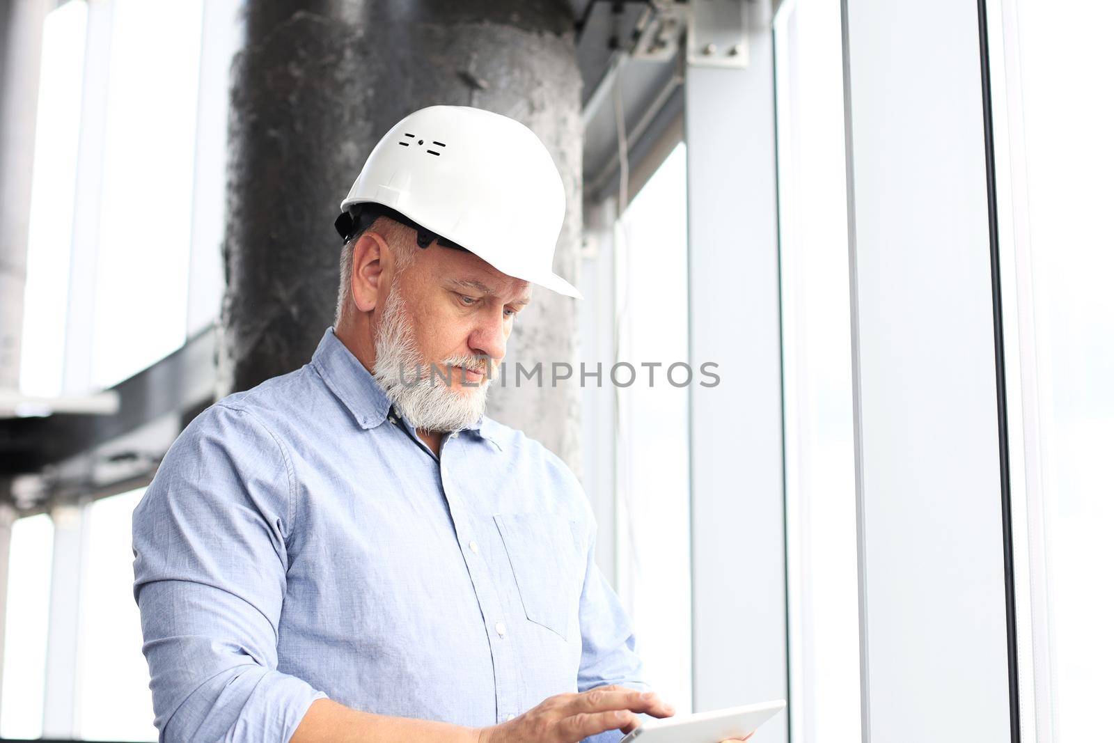 Mature architect wearing hardhat inspecting new building. by tsyhun