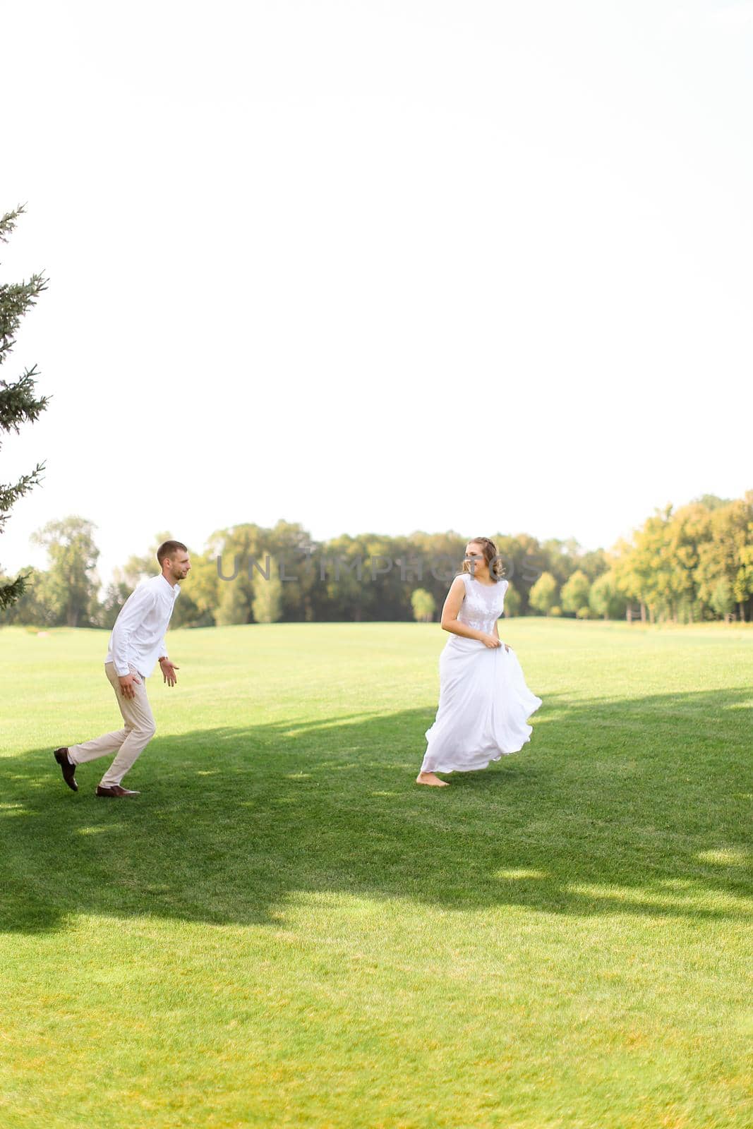 American groom and bride running and playing on grass. Concept of wedding photo session on open air and nature.