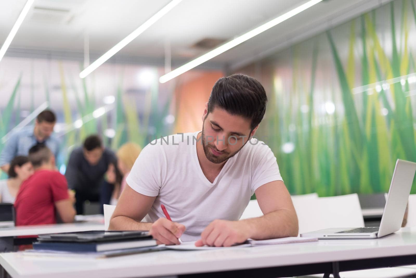 male student in classroom working  homework  and learning with laptop computer, students group in background