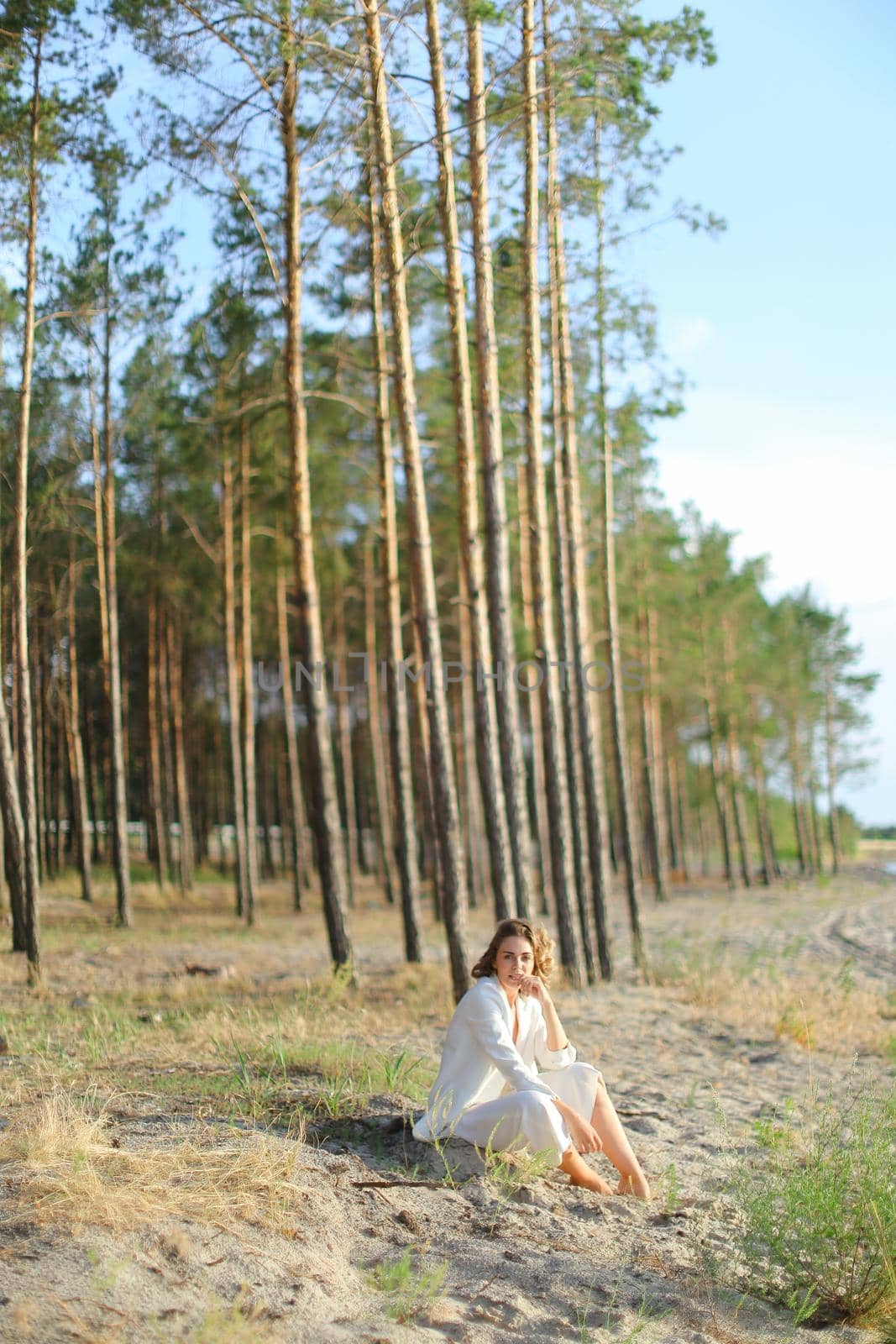 Young girl sitting on sand beach with trees in background. by sisterspro