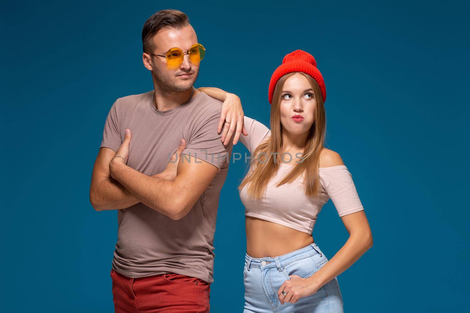 Studio lifestyle portrait of two best friends hipster wearing stylish bright outfits, hats, denim shorts and glasses, going crazy and having great time together. Indoor studio shot, isolated on blue background.