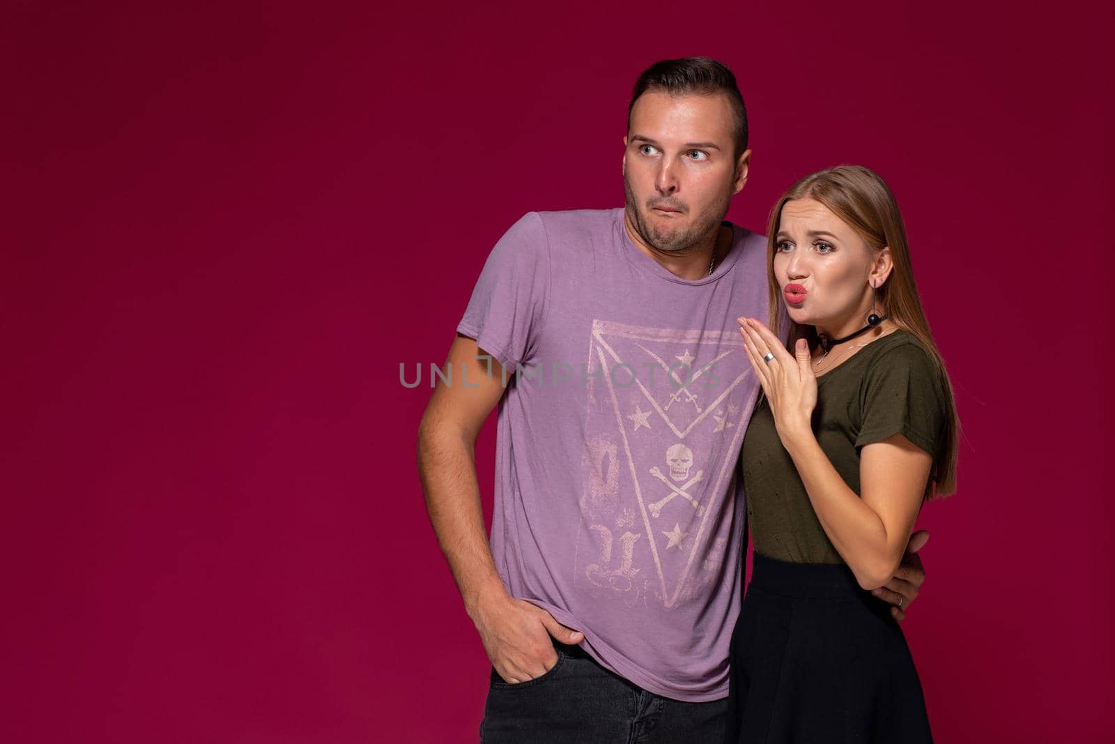 Unhappy discontent woman and man look with disgusting expression, as see something unpleasant. Friends express negative emotions and feelings, isolated over burgundy background. Awkward couple
