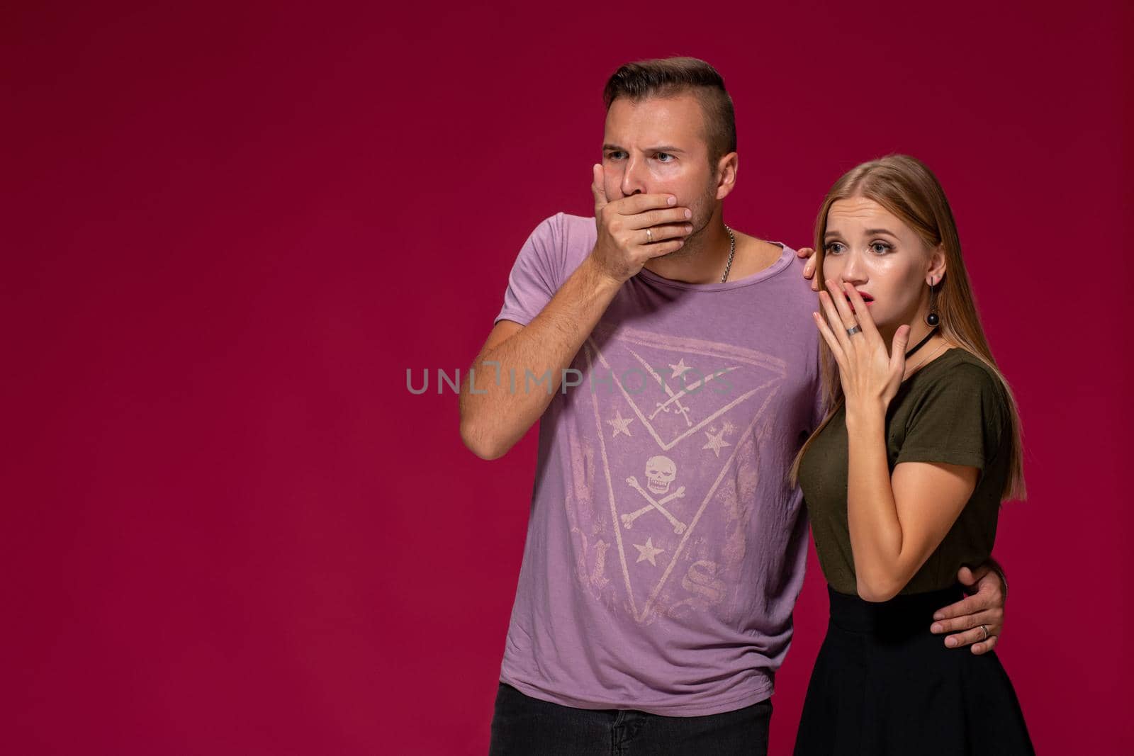 Unhappy discontent woman and man look with disgusting expression, as see something unpleasant. Friends express negative emotions and feelings, isolated over burgundy background. Awkward couple