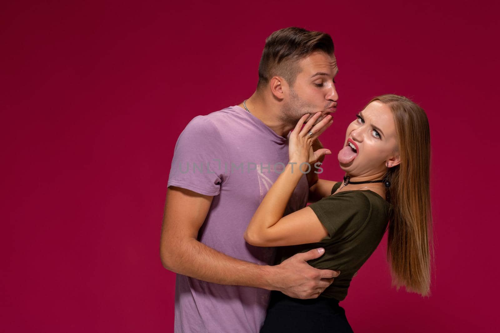 Portrait of outraged displeased woman gesturing to stop with hand while man trying to kiss her isolated over burgundy background