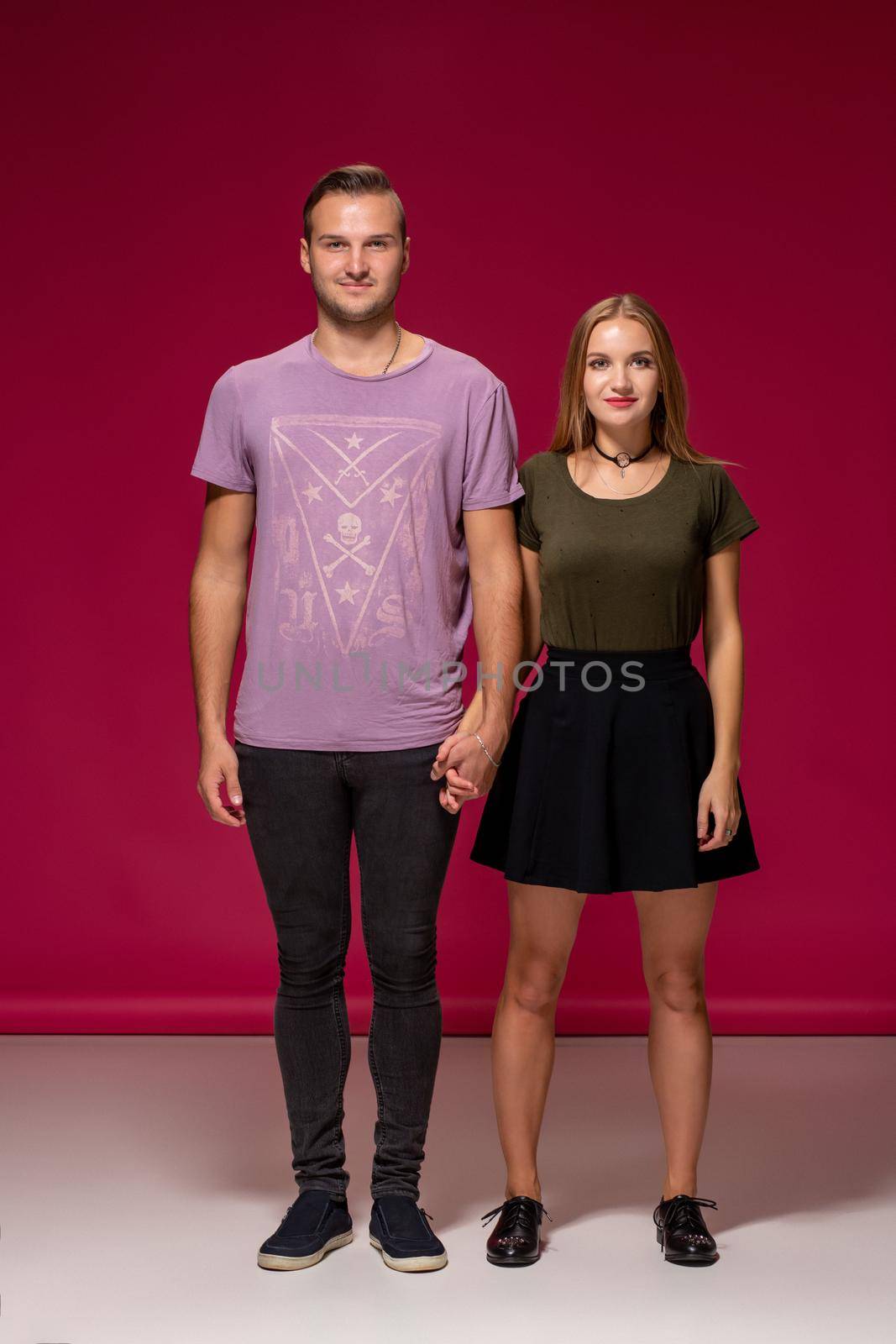 Totally in love. Full length of beautiful young couple embracing and smiling while standing against burgundy background with copy space for your advertisement or written text.
