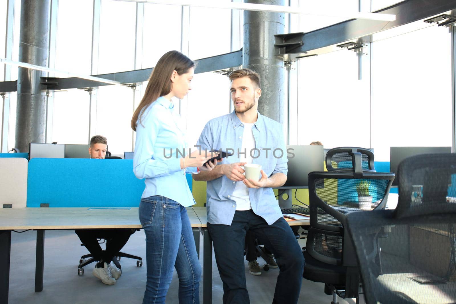 Two happy young people in casual wear smiling and looking at digital tablet while working together. by tsyhun