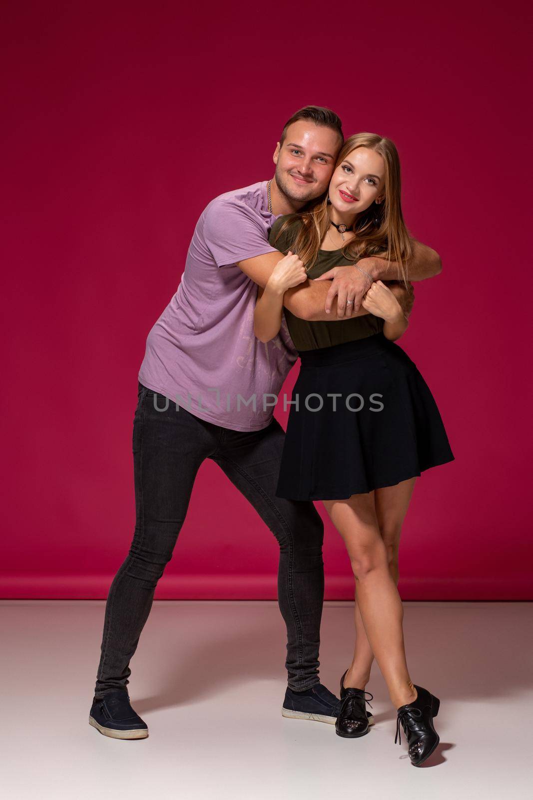 Totally in love. Full length of beautiful young couple embracing and smiling while standing against burgundy background with copy space for your advertisement or written text.