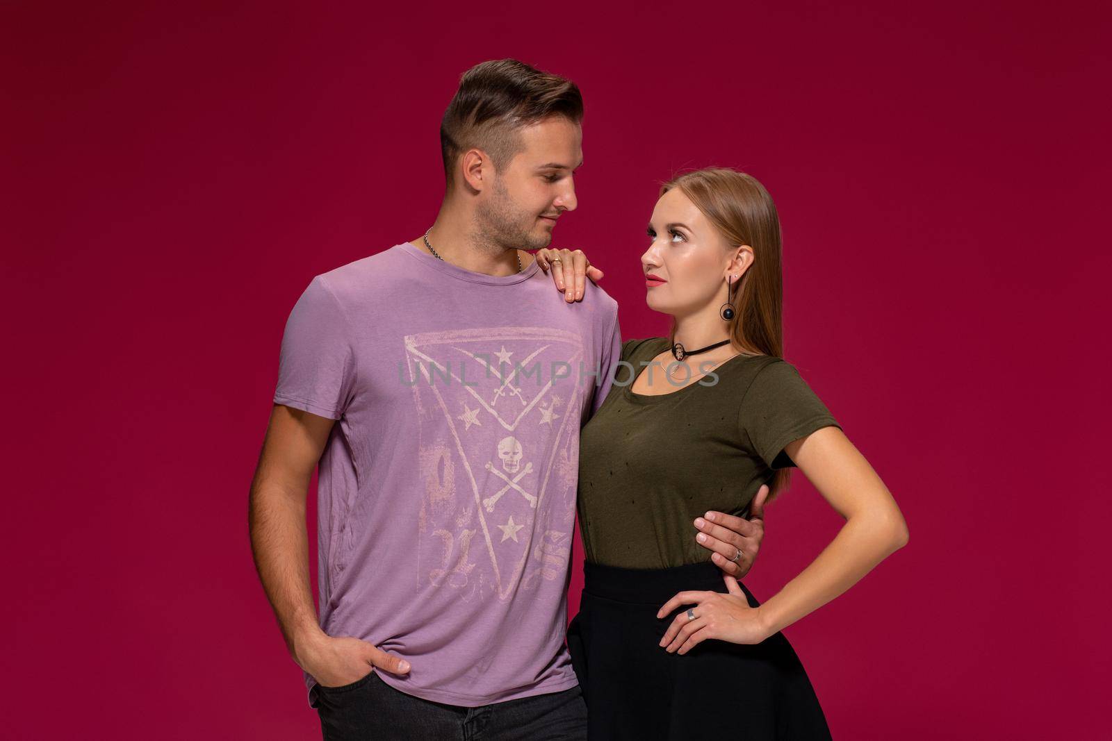 Young nice couple posing in the studio, express emotions and gestures, smiling, on a burgundy background with copy space for your advertisement or written text.