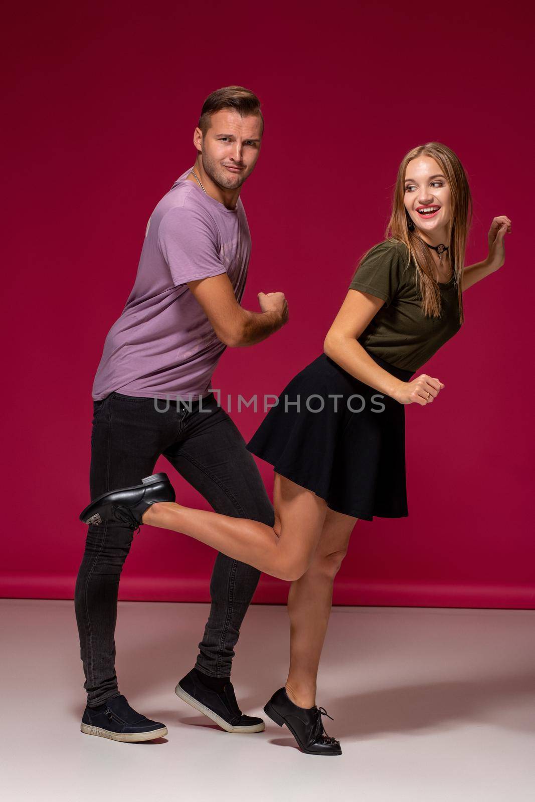 Totally in love. Full length of funny young modern couple dancing and having fun together over burgundy background