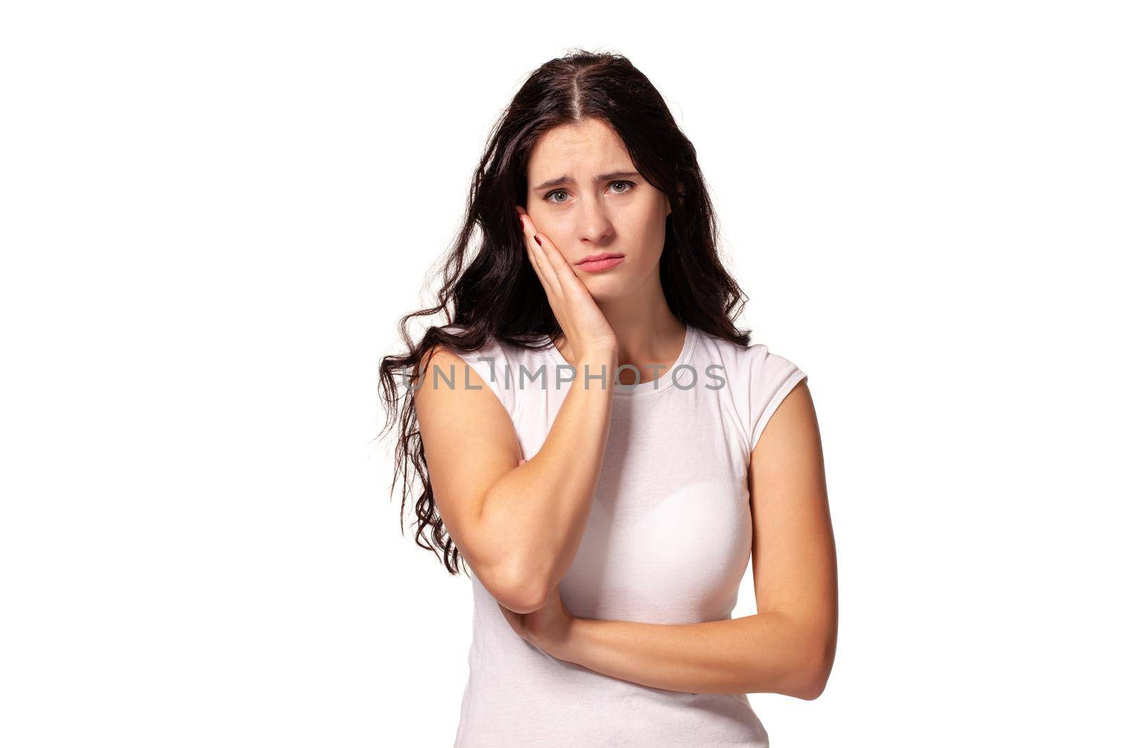 Beautiful and unhappy young woman with dark wavy hair looking into the camera with serious expression on her face. Isolated on white background.